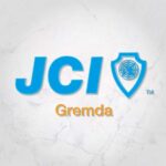 Un logo bleu et orange sur un fond marbré. Le logo est composé des lettres "JCI" et "GREMDA", ainsi que d'un globe terrestre stylisé.